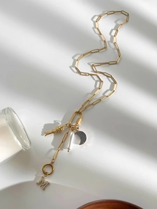 Detail van gouden M-letter hanger met kristallen en parels aan een geschakelde ketting