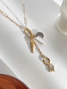 Detail van de gouden paperclip ketting met parel en kristallen M initiaal hanger