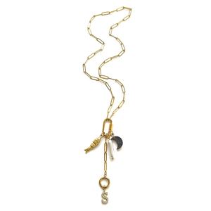 Detail van gouden paperclipketting met hangers van vis, parel, maan en de letter S