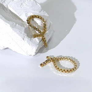 Minimalistische goldene Box-Ketten-Ohrringe auf weißem Fels mit Metallglanz