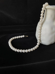 Close-up of elegant single-layer pearl necklace with golden clasp on black velvet