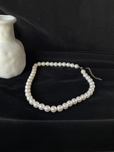 Close-up of elegant single-strand white pearl necklace with gold lobster clasp on black velvet