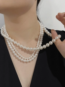 Detailed view of elegant triple-layered pearl necklace worn on a black V-neck top