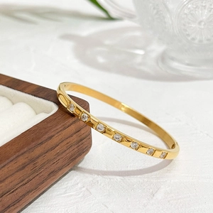 Gold plated titanium steel bangle with inlaid zircons on a walnut jewelry display