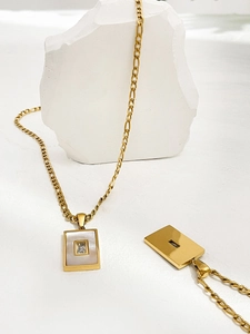 Detailopname van de gouden rechthoekige hanger met parelmoer inleg en witte zirkoon