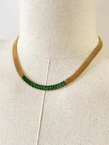 Detalle de collar de malla dorada con circonitas verdes rectangulares de estilo retro