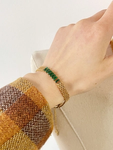 Detalle de una pulsera de malla dorada con cinco piedras verdes rectangulares de mujer