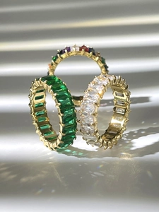Detailaufnahme goldener Eternity-Ringe mit smaragdgrünen und bunten Zirkon-Steinen im Sonnenlicht