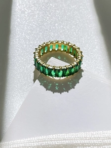 Nahaufnahme von Gold-Titan-Eternity-Ring mit rechteckigen grünen Zirkonia-Steinen