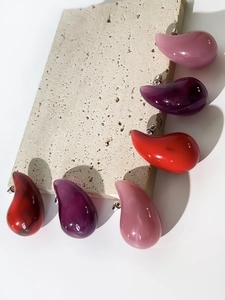 Detail shot of colorful teardrop acrylic stud earrings on a textured stone surface