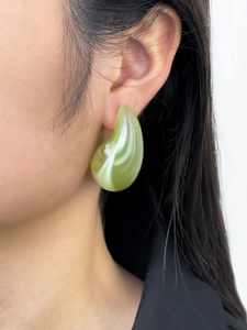 Close-up of a large drop-shaped acrylic earring with green marble texture on a model