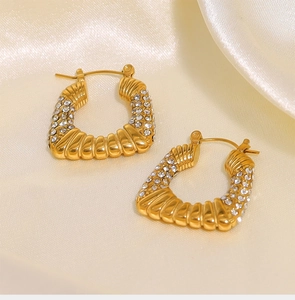 Detalle de pendientes de aro dorados de acero de titanio con textura plisada y circonitas
