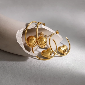 Polished gold heart and sphere drop earrings displayed on a minimalist sculpture
