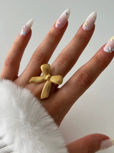 Detailed close-up of a 18K gold bow-shaped ring with textured ribbon design on a finger