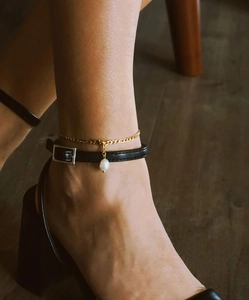 Detalle de una cadena de titanio dorado con perla de agua dulce en el tobillo de la modelo