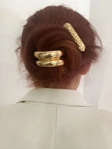 Dettaglio di due accessori per capelli in metallo dorato con texture lisce e martellate su modella
