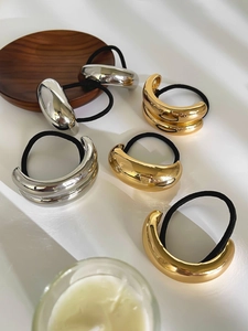 Dettaglio ravvicinato di elastici per capelli minimalisti in metallo dorato e argento a C