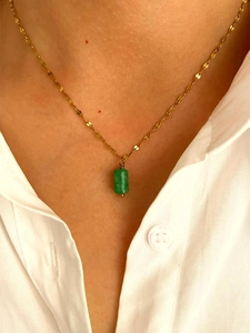 Close-up of a gold necklace with a green cylindrical stone pendant worn on a white shirt