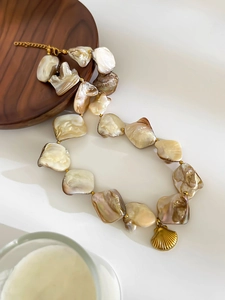 Macro view of Baroque pearl necklace with gold shell pendant on wooden tray