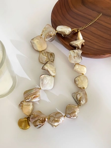 Detail of irregular shell pearl necklace with gold shell pendant on wooden tray