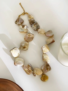 Detail shot of natural shell shards and a golden scallop pendant on a waterproof steel chain