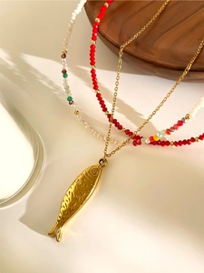 Detalle del colgante de pez dorado y collares de cuentas acrílicas en una bandeja de madera