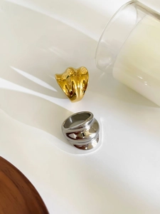 Detailed view of high-polished gold and silver wide wavy rings on a minimalist surface