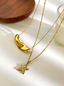 Detail of gold double-layered necklace with star pendant and sleek bean charm on beads chain