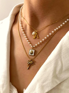 Dettaglio della collana a tre strati dorata con ciondoli a conchiglia, perla e palma
