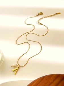 Dettaglio della collana dorata con ciondolo lettera A, piccola perla e chiusura a moschettone