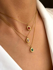 Close-up of layered 18K gold-plated necklaces with oval emerald, red, and purple gemstones