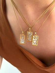 Detail of three vintage gold rectangular necklaces with white shell and tarot symbols