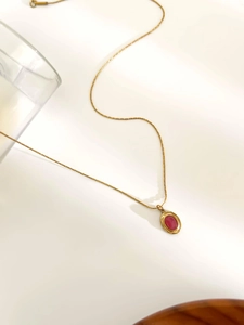 Detail of 18K gold stainless steel necklace with oval red stone pendant on white surface