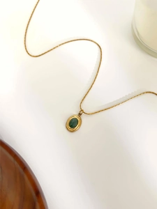 Detail of 18K gold necklace with oval green natural stone pendant on white background