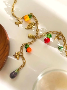 Detailansicht der goldenen Y-Kette mit bunten Obst- und Insektenanhängern auf weißem Grund