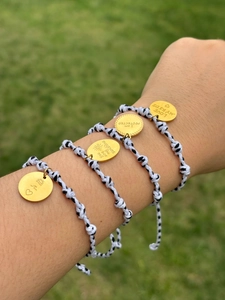 Détail de bracelets tressés ajustables avec breloques dorées gravées au poignet