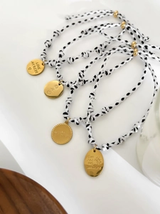 Détail de cordons tressés réglables avec charms gravés en acier inoxydable doré sur bois