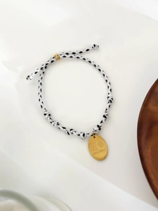 Détail du bracelet en corde tressée avec un pendentif ovale doré gravé d'un soleil