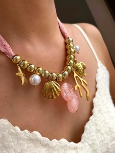 Dettaglio di collana intrecciata rosa con ciondoli dorati a forma di stella marina e tartaruga