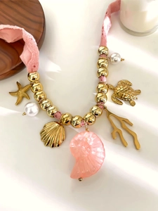 Dettaglio macro di ciondoli a conchiglia e stella marina su collana intrecciata rosa