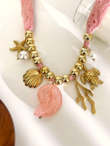 Dettaglio collana in pizzo rosa con stelle marine, conchiglie e tartaruga dorata