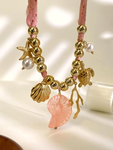 Primo piano della collana in corda intrecciata rosa con ciondoli dorati a forma di stella