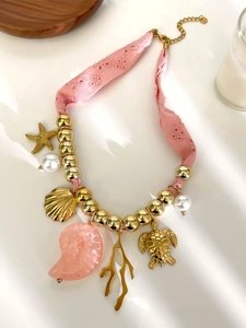 Dettaglio collana in pizzo rosa con pendenti conchiglia dorata stella marina e resina