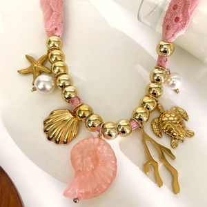 Collana in pizzo rosa intrecciato con ciondoli dorati a forma di stella marina e tartaruga