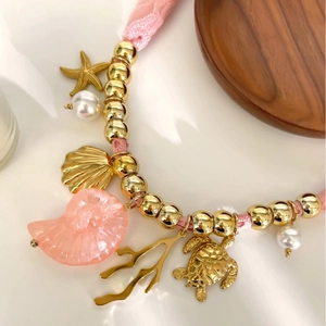 Collana in pizzo rosa con ciondoli a forma di stella marina dorata, tartaruga e conchiglia