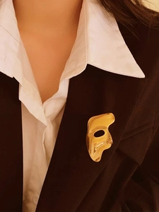 Detail of a gold Phantom style mask brooch pinned on a white shirt and black suit