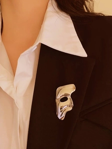 Polished silver mask brooch with an artistic opera design on a dark suit lapel