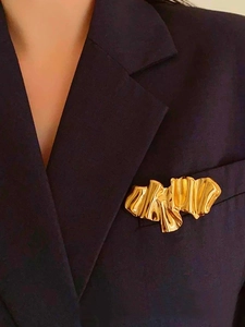 Macro shot of abstract folded golden metal brooch on a dark blue suit lapel