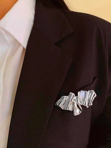 Close-up of a silver abstract wave brooch with mirror finish on a black suit lapel