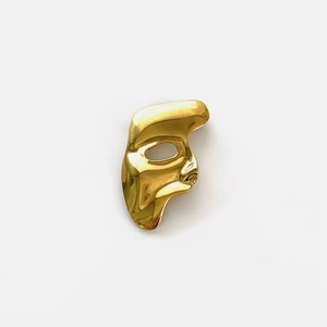 Detail of creative half-face mask brooch in polished gold finish with mirror effect